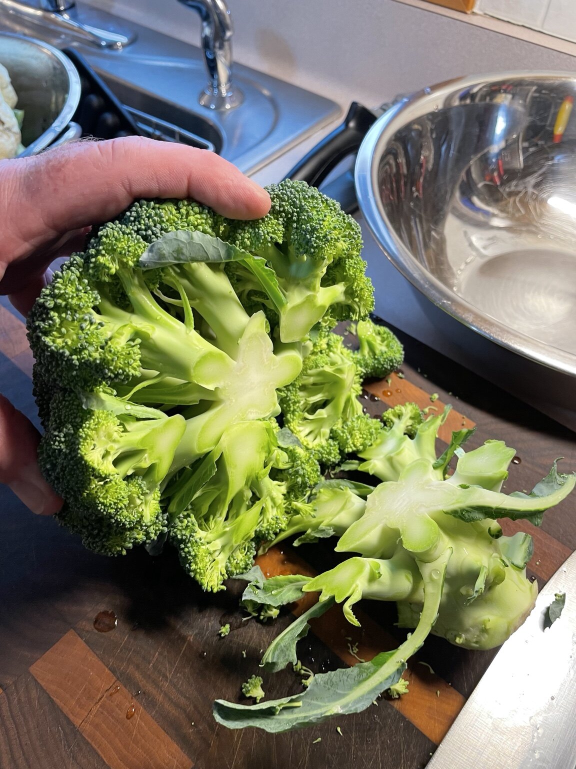 Broccoli being trimmed from the stem side with a sharp chef's knife