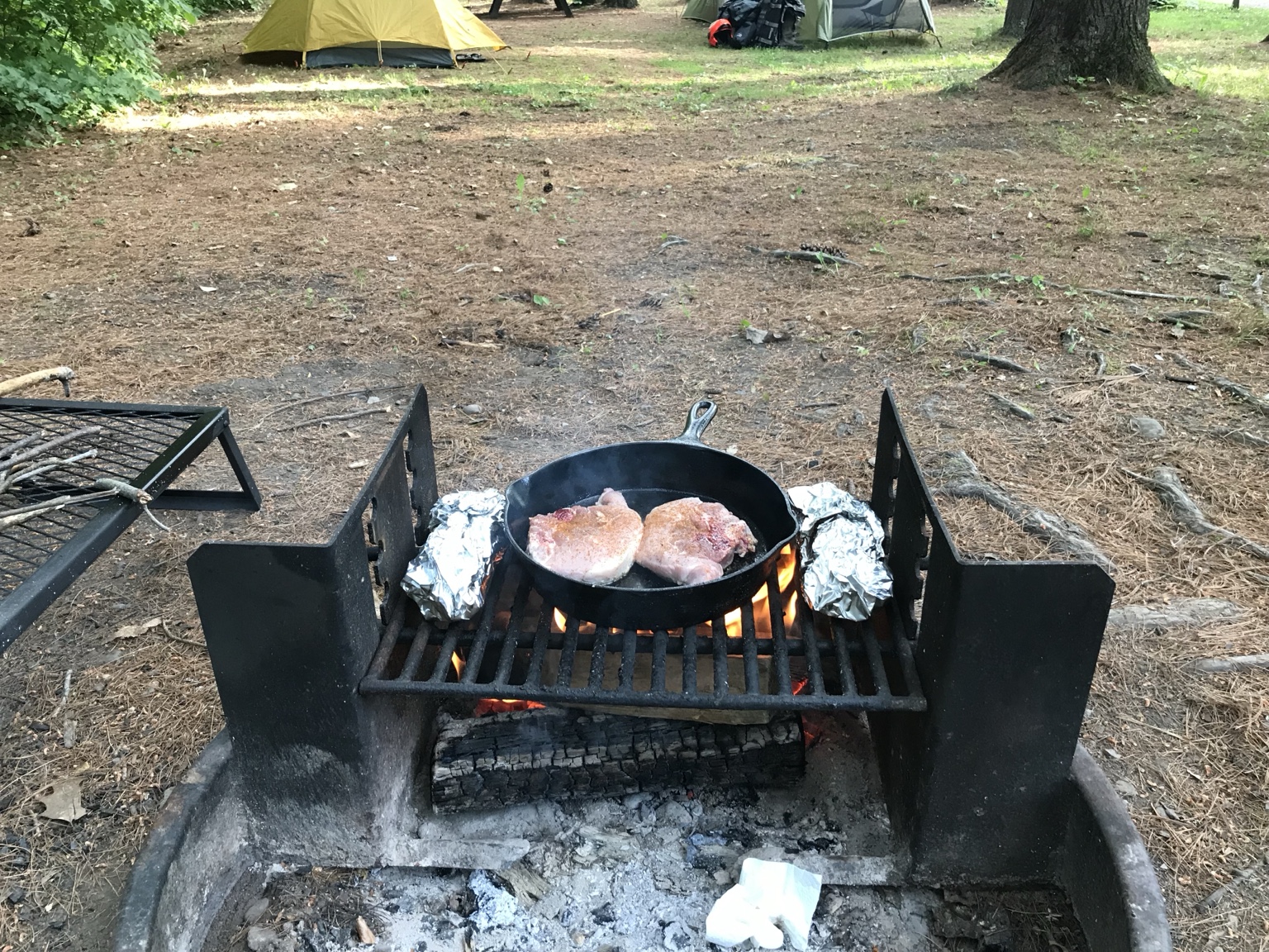 Pork chops cooking in cast iron over a campfire