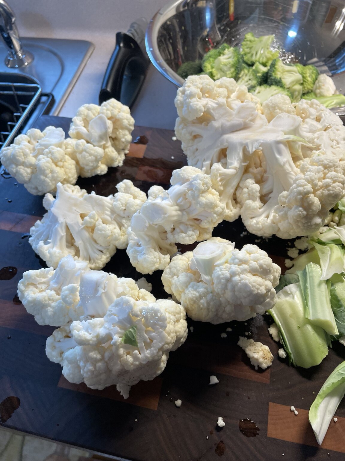 Cauliflower broken into florets on a butcher-block cutting board