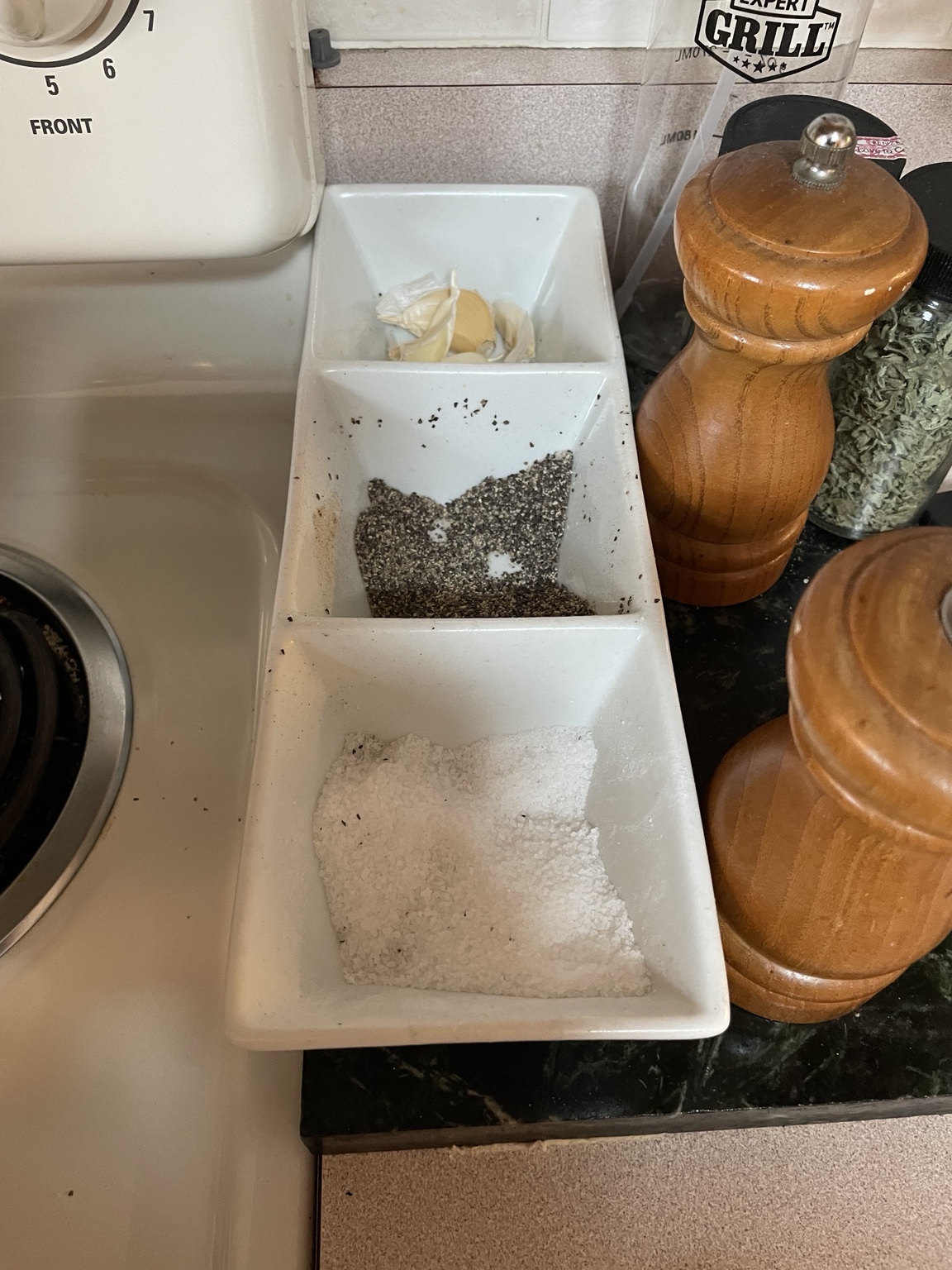 Kosher salt, coarse black pepper, garlic, and wooden mills beside the stove